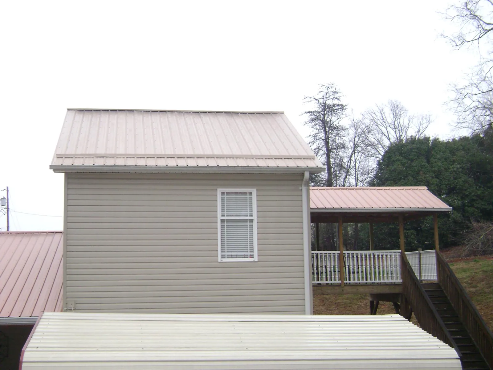 Tan metal roofs on a two story addition and attached porch, from a Roof Replacement job in Stockport